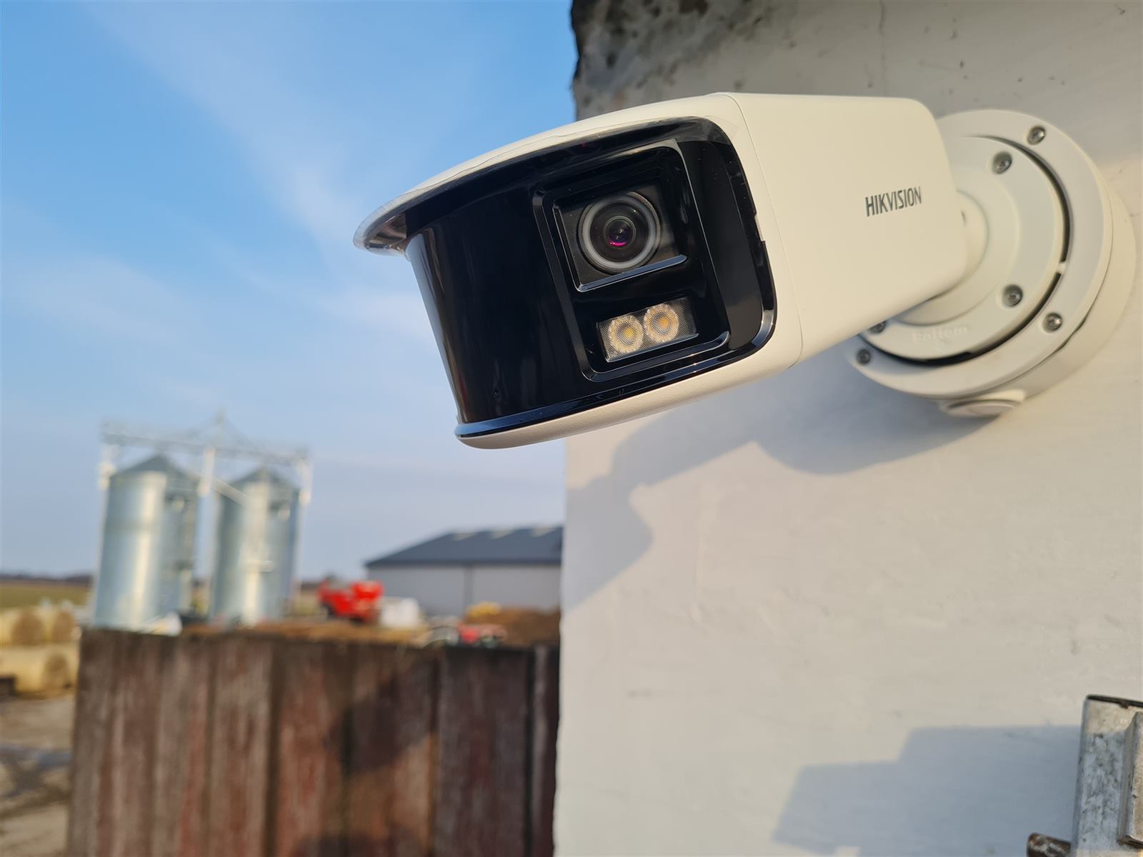 Panoramiczna kamera Hikvision na budynku gospodarczym, w tle silosy i hala